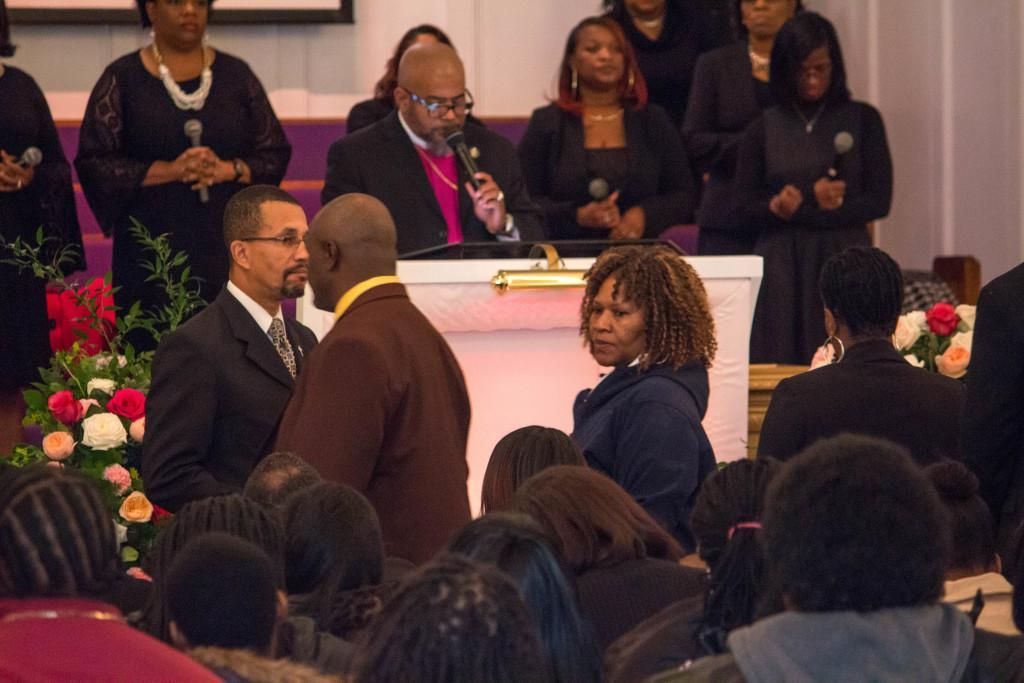 People at a church service. A man speaks into a microphone. Others stand, some hold microphones.