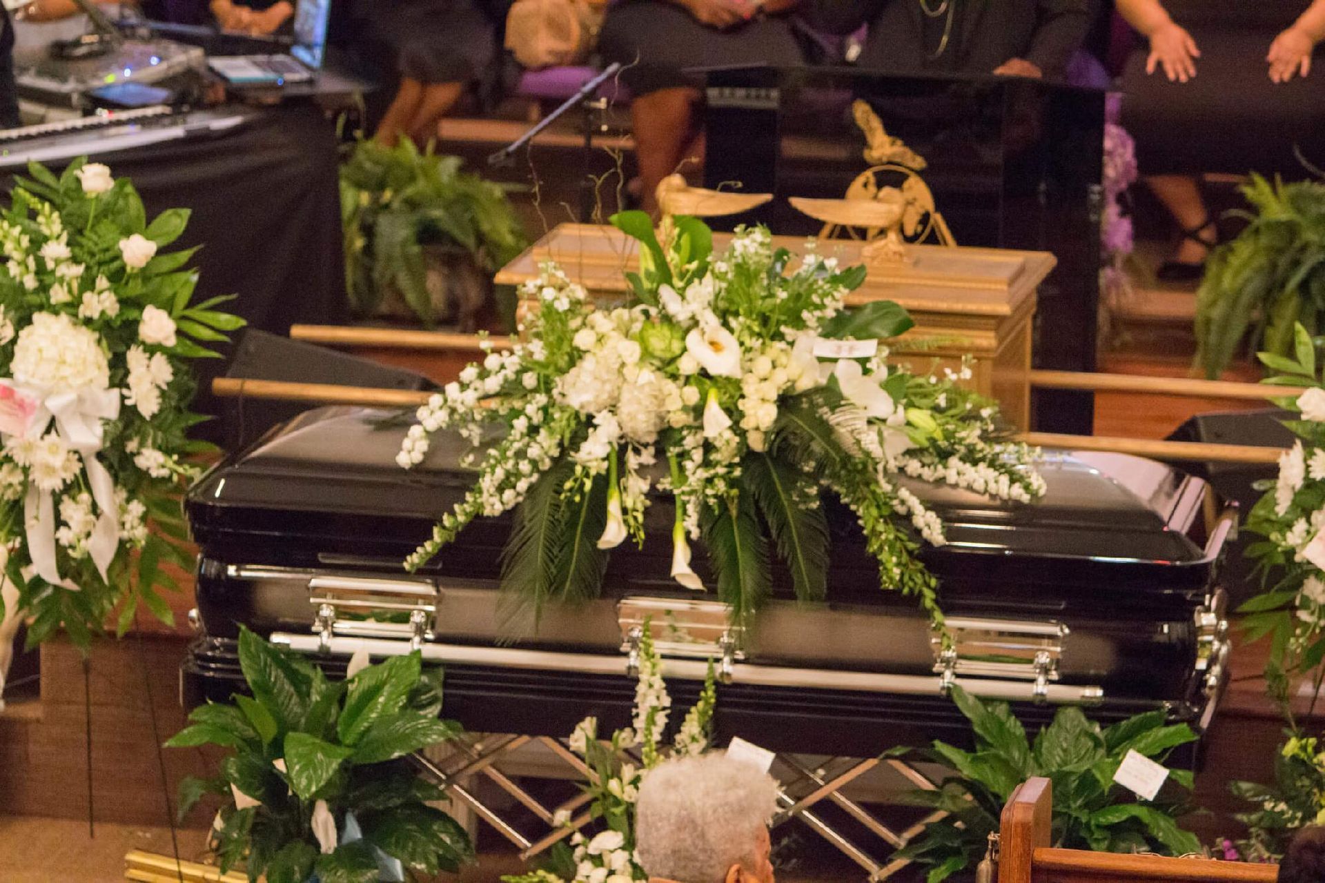 Black casket with white floral arrangement in a church setting.