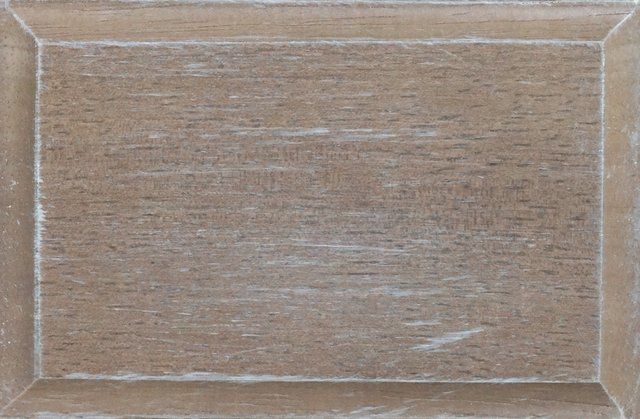 Close-up of a wooden cabinet door with a weathered, light brown finish and a white painted border.