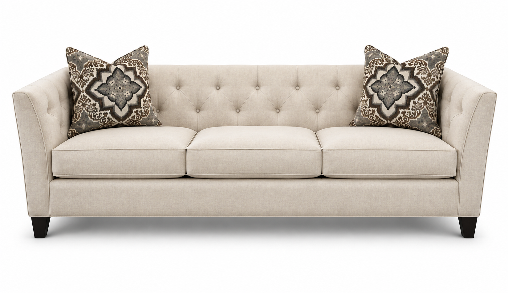 Beige tufted sofa with two patterned throw pillows on a white background
