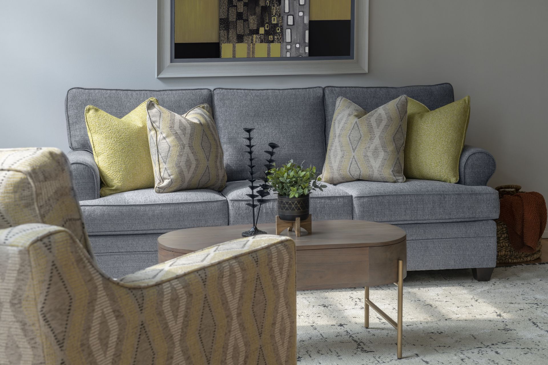 A living room with a couch , chair , coffee table and painting on the wall.
