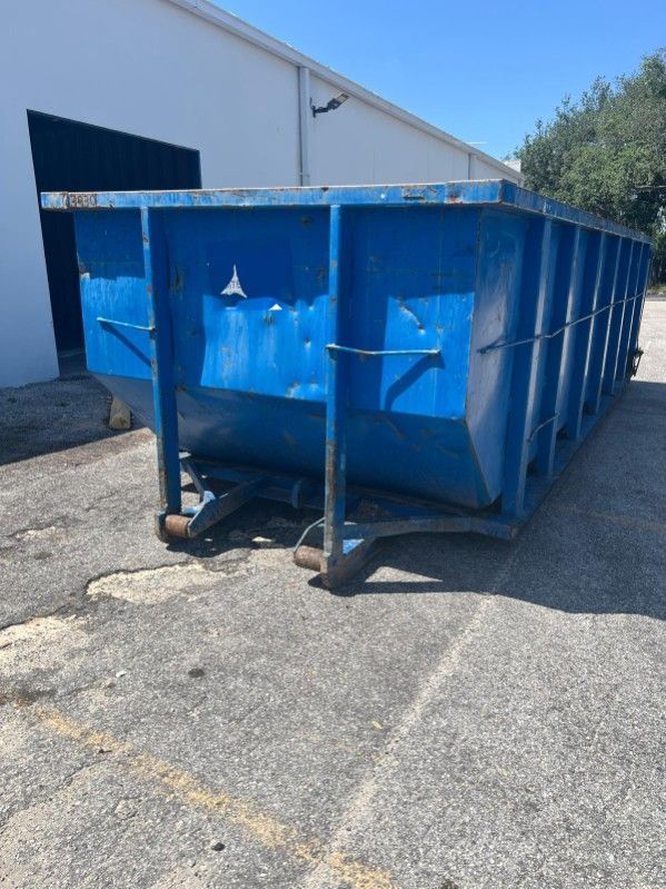 Blue industrial dumpster on a paved lot beside a warehouse building.