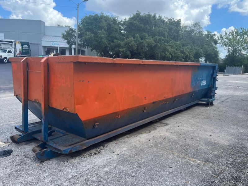 Large orange and blue industrial dumpster on a gravel lot under a partly cloudy sky