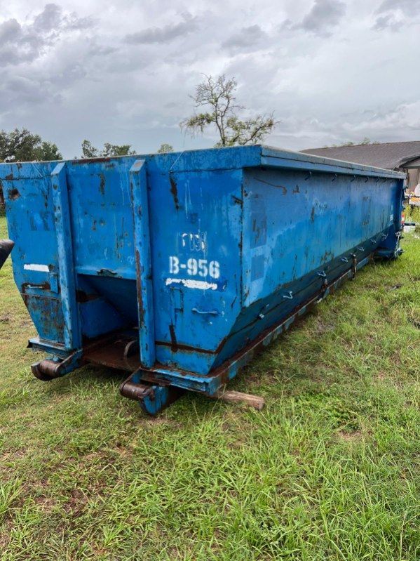 Blue metal dumpster on grassy ground under a cloudy sky