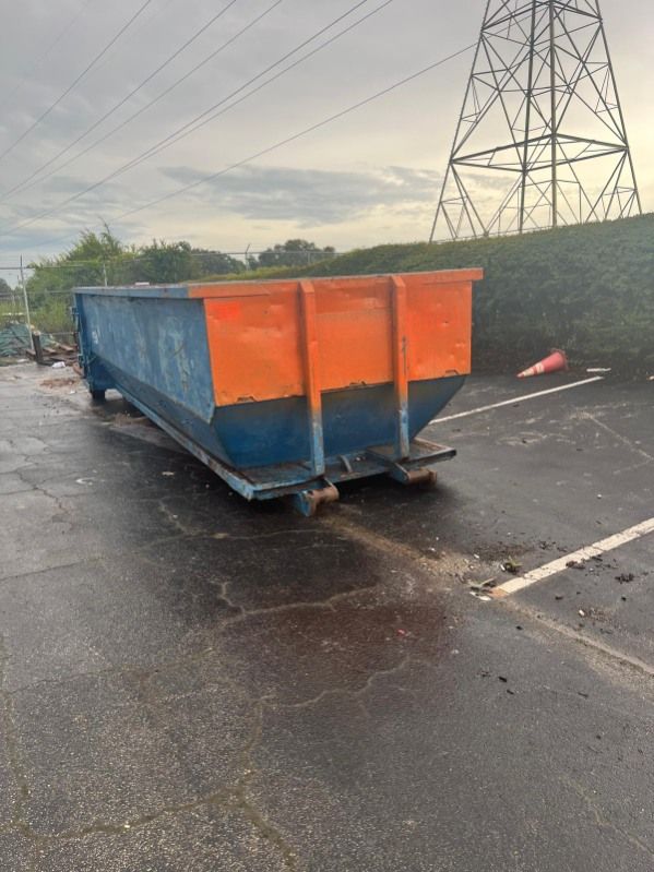 Blue-and-orange dumpster on wet pavement near power lines under a cloudy sky