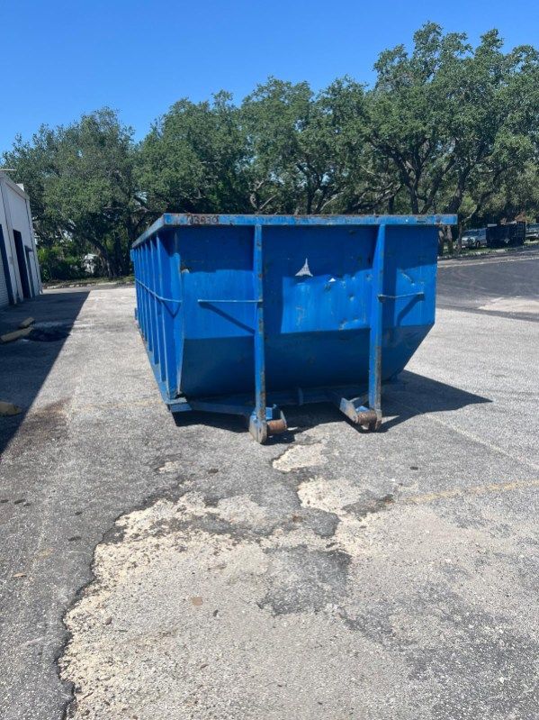 Blue dumpster on cracked asphalt in a sunny parking lot.
