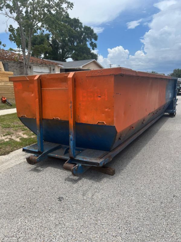 Large orange and blue metal dumpster on a residential street under a partly cloudy sky