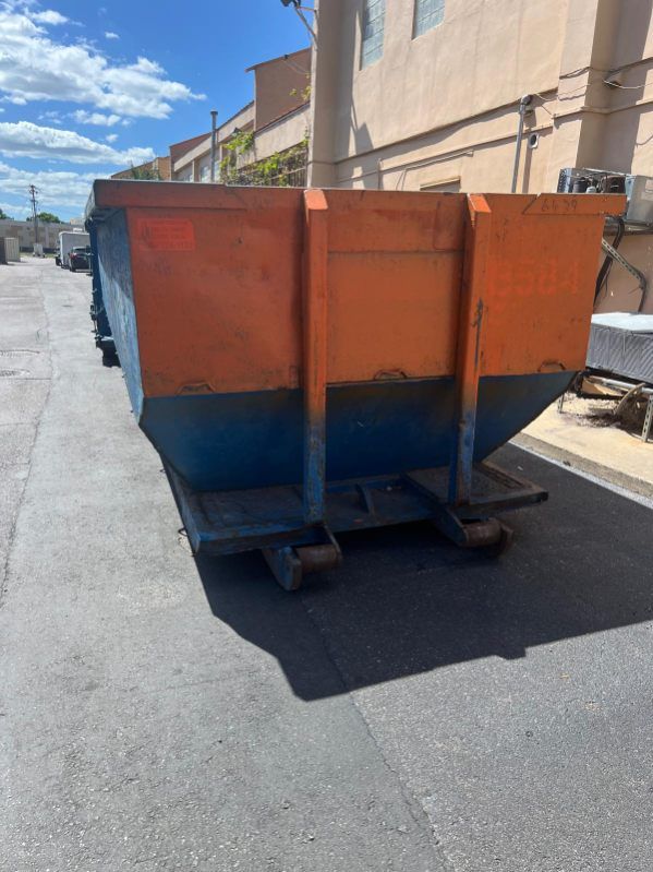 Orange and blue metal dumpster on a street beside a beige building