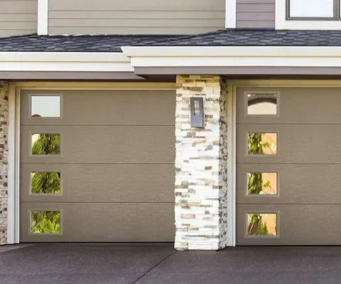 Tan garage doors with square windows, set in a two-car garage with a stone column, under a beige-trimmed roof.