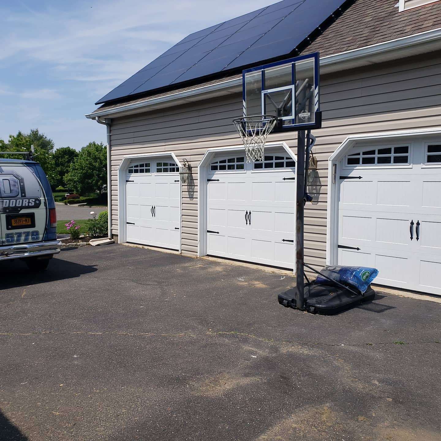 Three-car garage with basketball hoop in driveway; a van is parked on the left. Solar panels are on the roof.