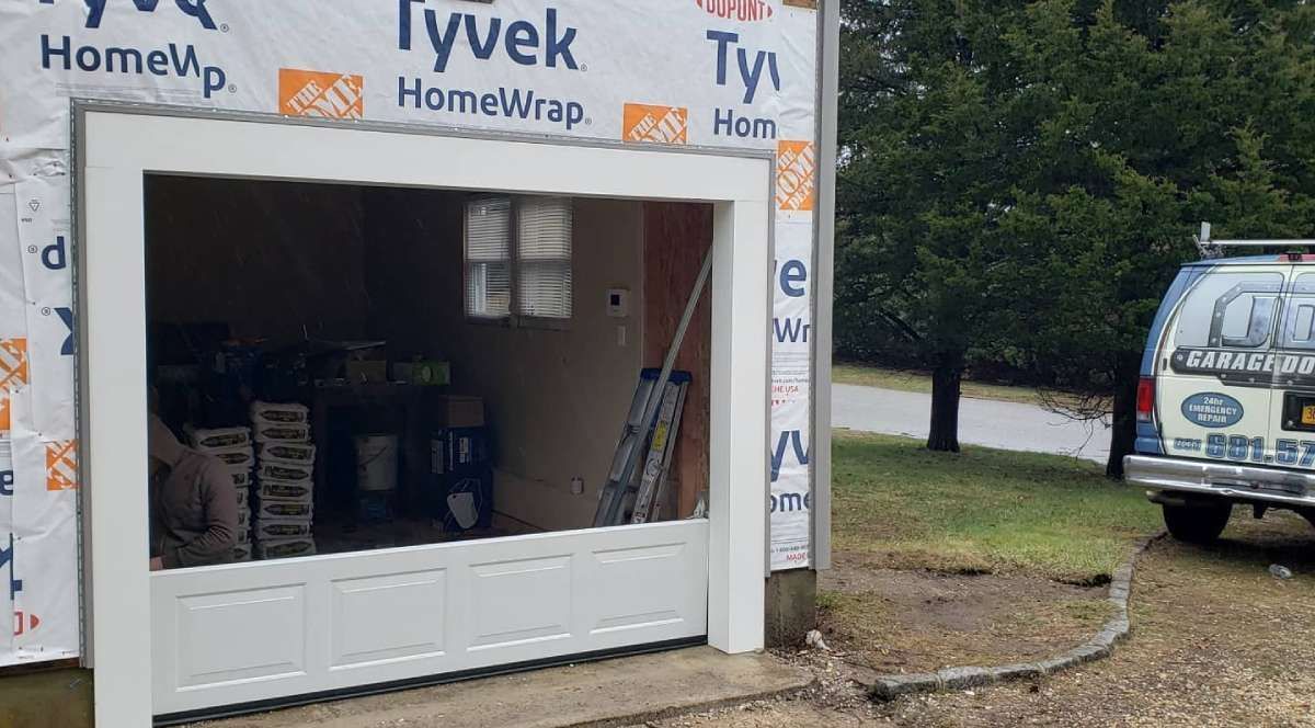 White-framed garage door opening under construction, covered with Tyvek. A van is parked to the right.