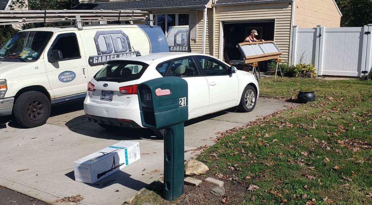 White car parked in driveway with a utility van and open garage. A mailbox is in the foreground.