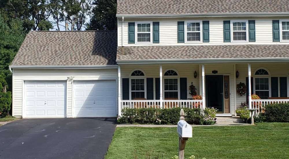 Two-story house with a white exterior, green shutters, and a two-car garage. A porch with a white railing and a green lawn.