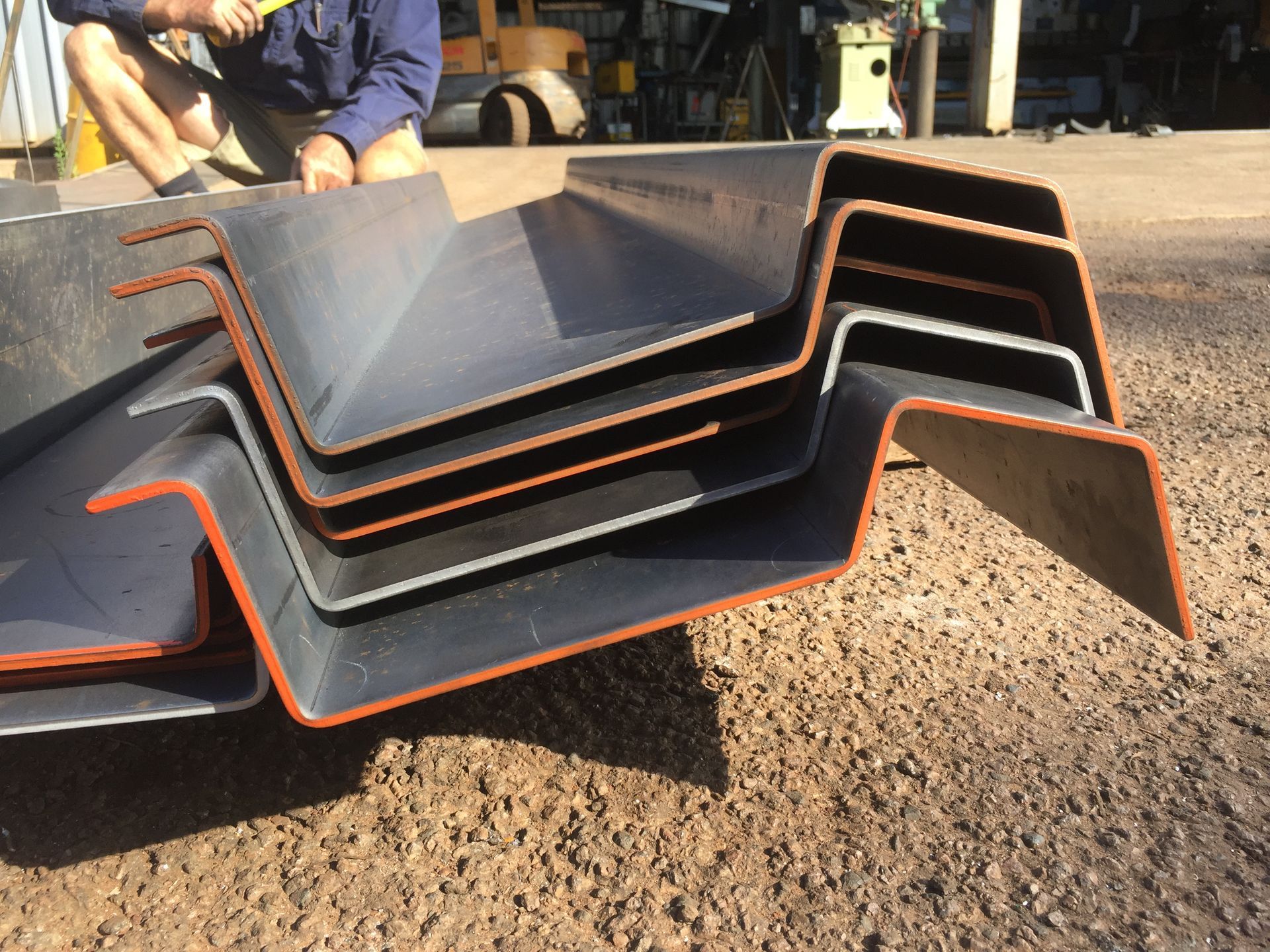 Stacked Black and Orange Metal Ramps on Gravel With a Man Working in the Background — Greville Fabrication in Girraween, NSW