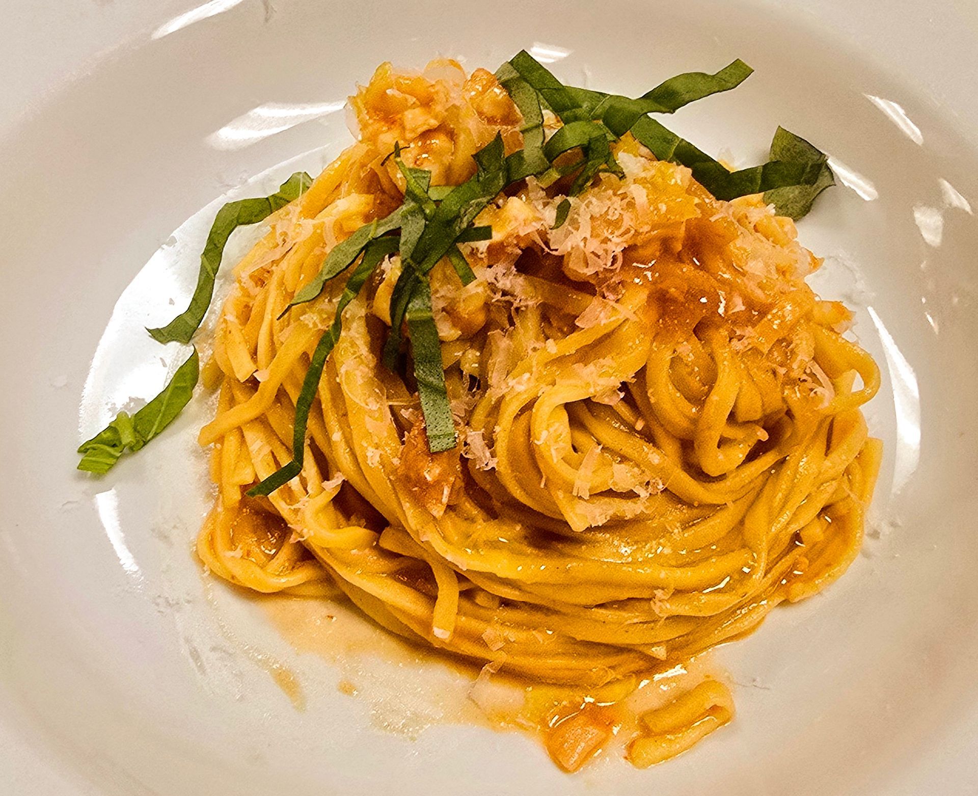 Pasta dish with orange sauce, basil garnish, and grated cheese in a white bowl.