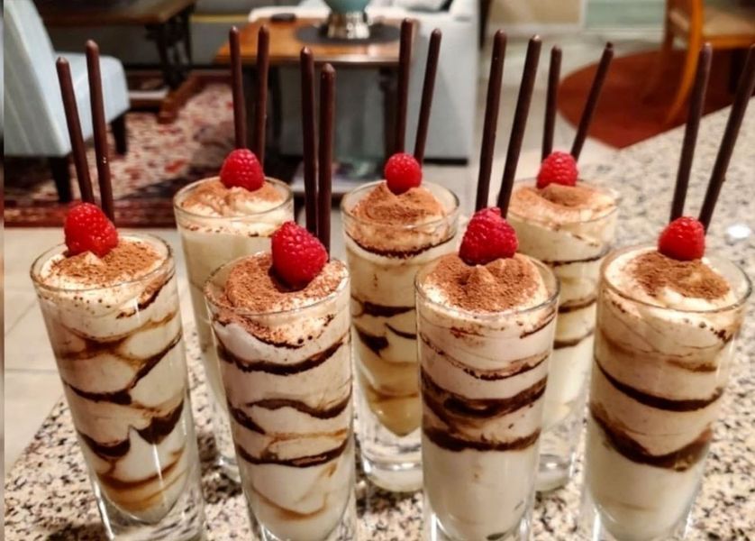 A row of shot glasses filled with desserts with raspberries on top.