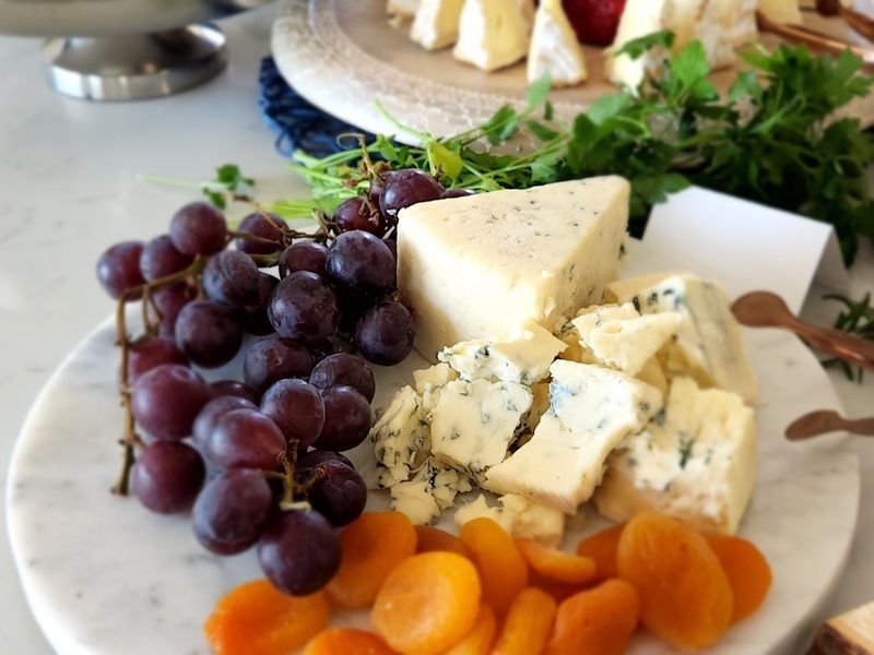 A plate of cheese grapes and apricots on a table