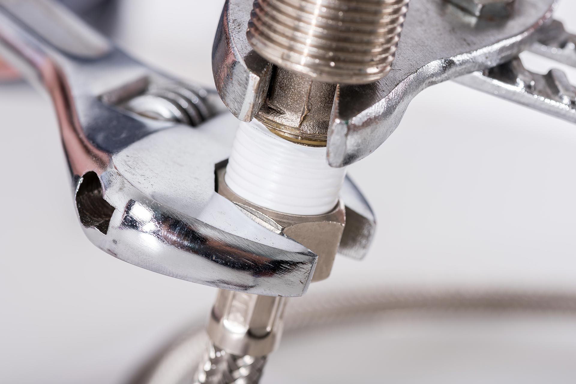 Close-up of a plumbing connection with threaded pipe wrapped in tape and tightened with a wrench.
