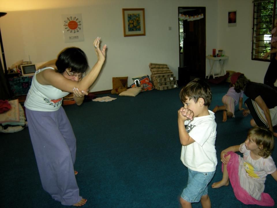 A woman in purple pants is dancing with two children