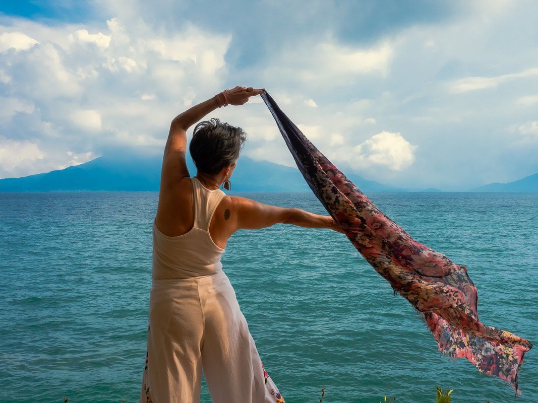 A woman is holding a scarf in front of the ocean.