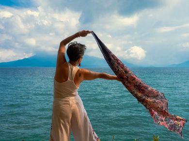A woman is holding a scarf in front of the ocean.