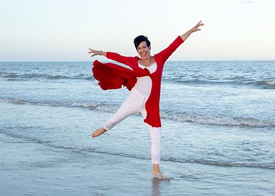 A woman in a red dress is dancing on the beach