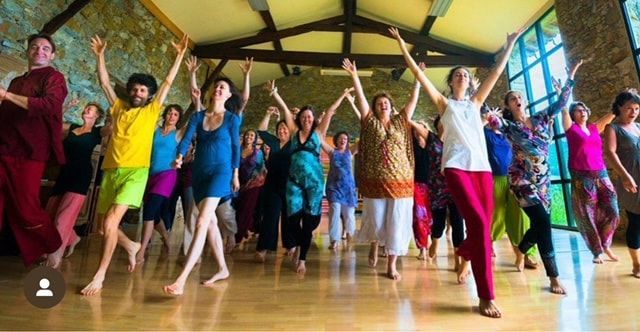 A large group of people are dancing in a room with their arms in the air.