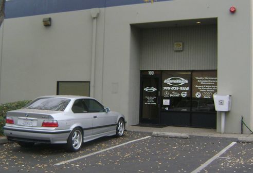 Silver sedan parked outside a gray commercial building entrance with glass doors and signs. | Eurotech Automotive