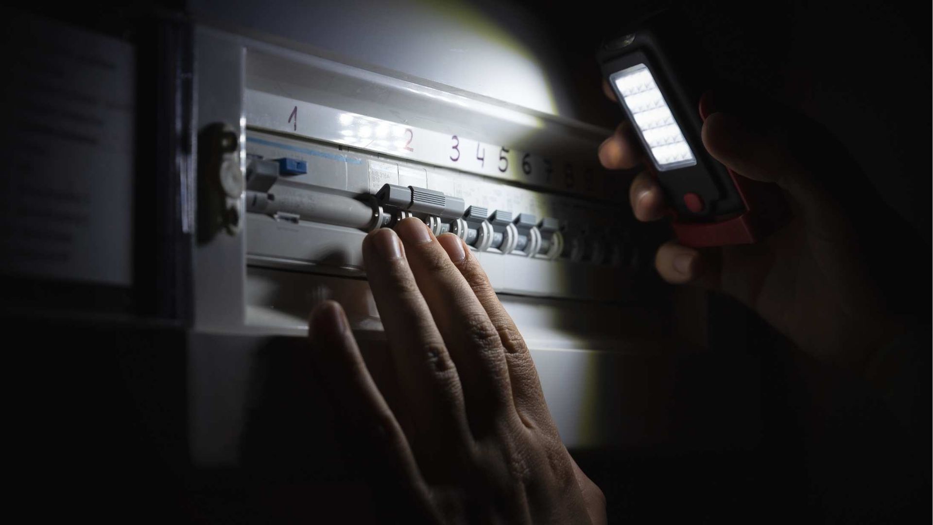 A person is looking at an electrical box with a flashlight.