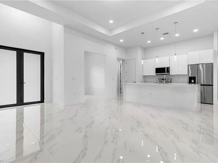 Amplia cocina moderna con pisos de mármol blanco, gabinetes blancos y electrodomésticos de acero inoxidable.