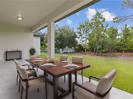 Comedor exterior cubierto con mesa de madera, seis sillas y vista a un patio con césped y árboles.