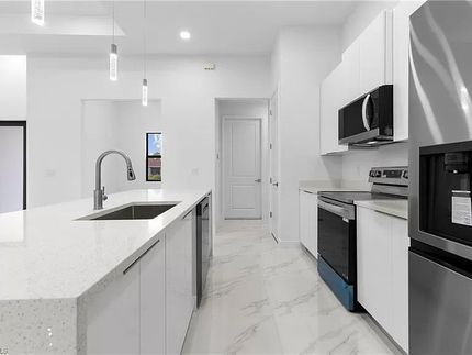 Cocina blanca moderna con isla, electrodomésticos de acero inoxidable y luces colgantes.