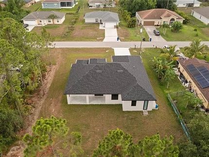 Vista aérea de una casa de un solo piso con techo oscuro en un terreno cubierto de césped, rodeada de árboles y casas suburbanas.