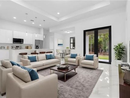 Moderna sala de estar con sofás neutros, almohadas azules y cocina abierta, puertas corredizas de vidrio al exterior.