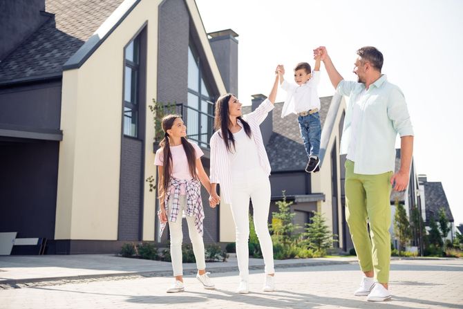 a family is standing in front of a house holding hands .