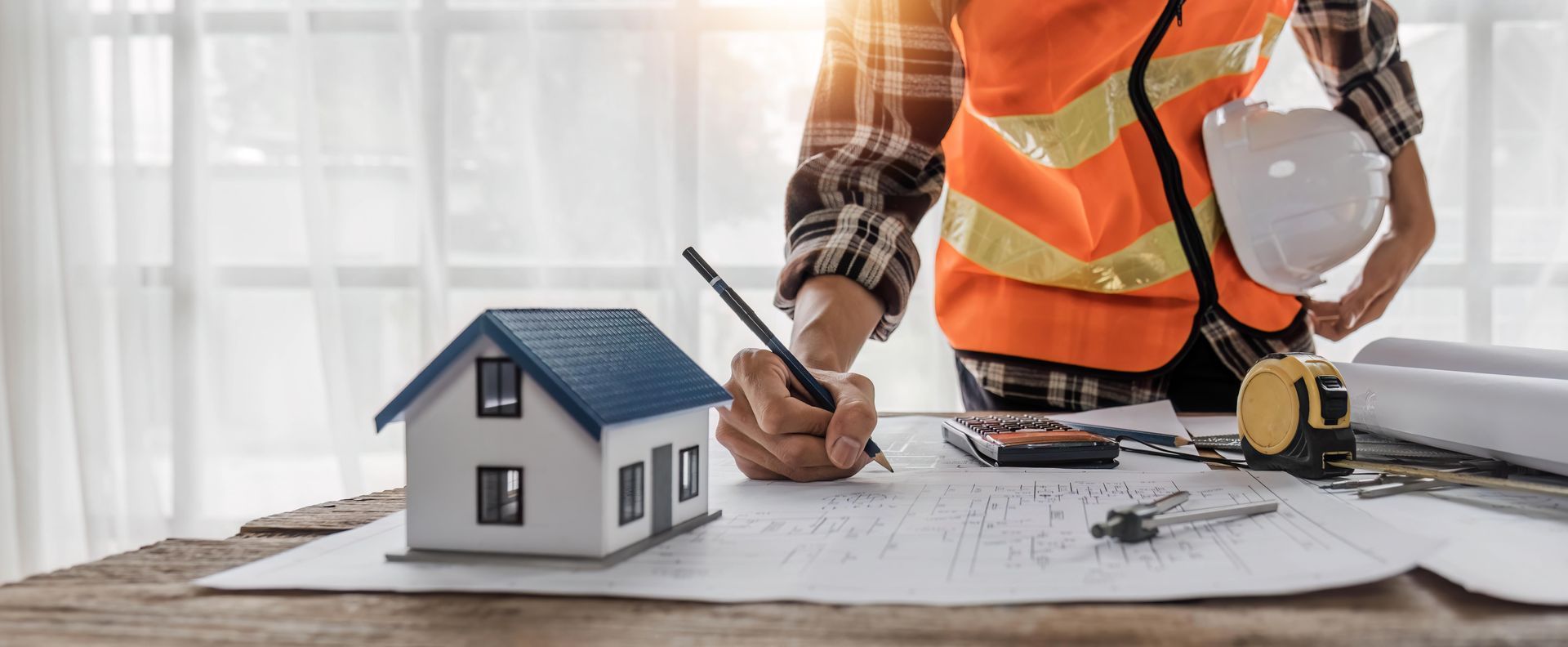 a construction worker is sitting at a table drawing a house on a blueprint .