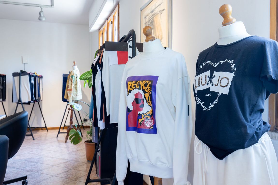 Boutique di abbigliamento con t-shirt grafiche esposte su manichini e appendiabiti in una stanza luminosa.