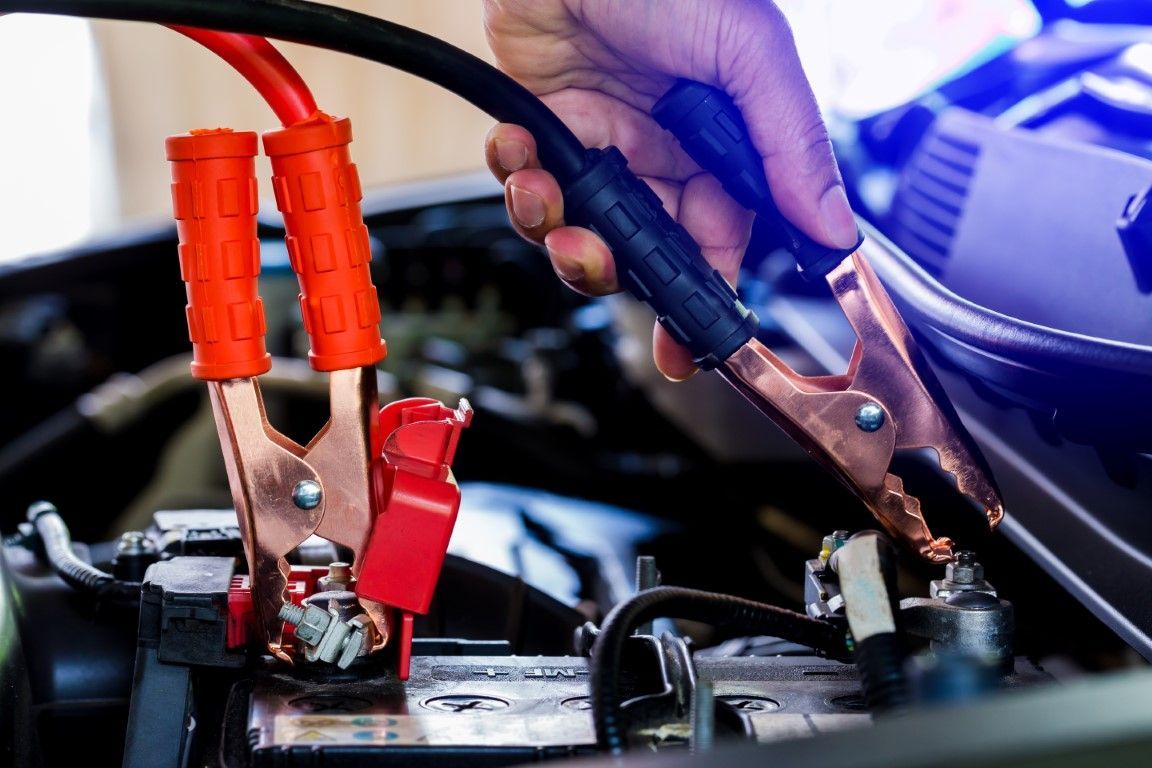 Jumper cables connecting to a car battery, held by a person's hand, ready to jumpstart a vehicle.