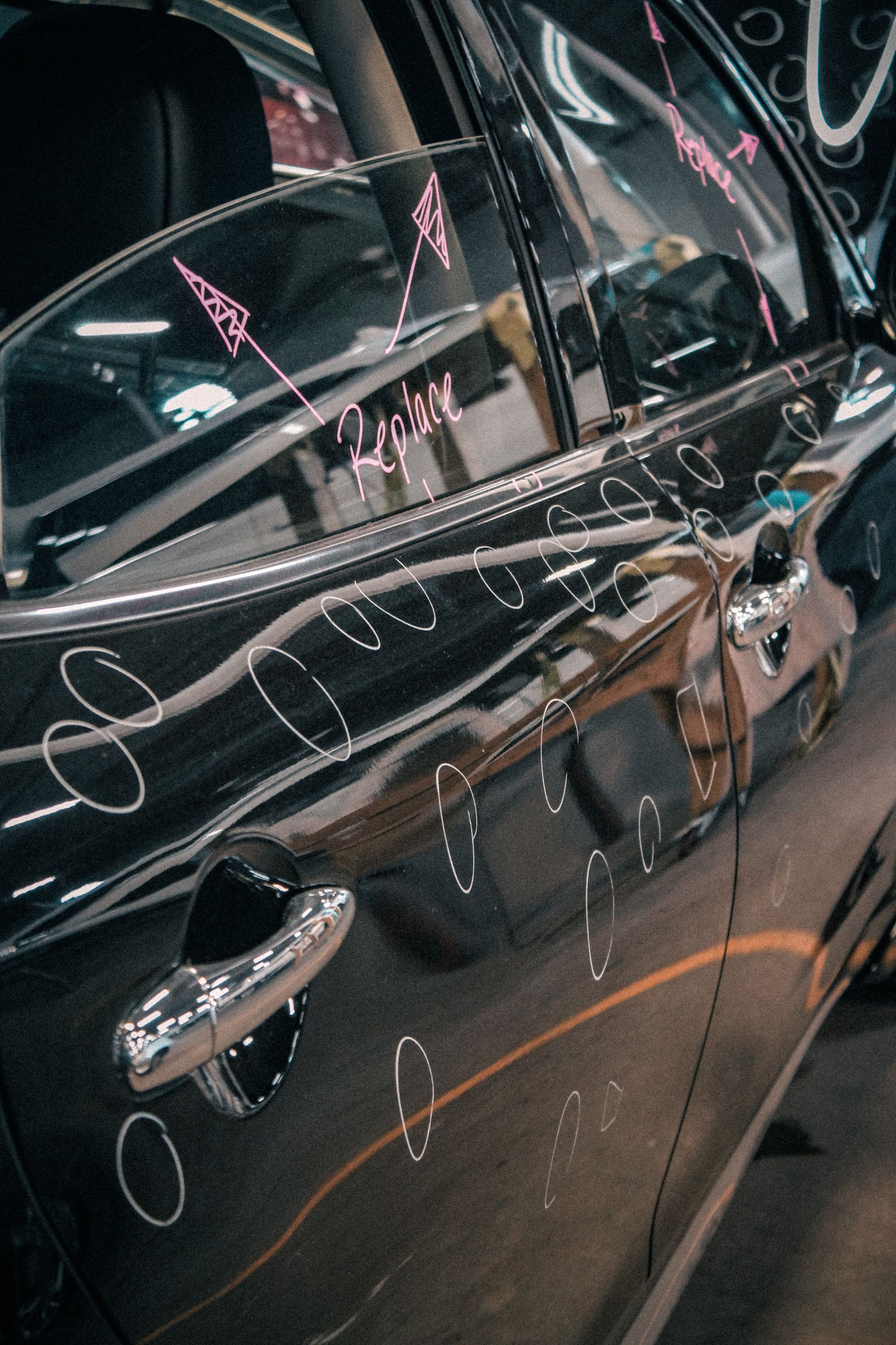 Dark car door with abstract white markings and reflections on glossy black paint