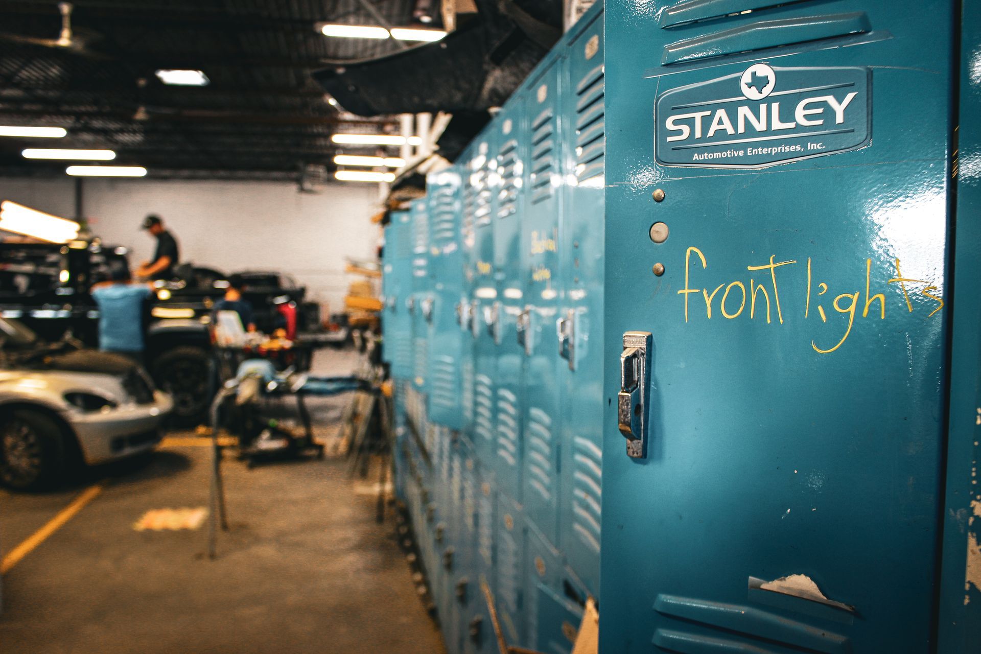 Blue Stanley tool lockers in an auto repair shop, with cars and mechanics in the background.