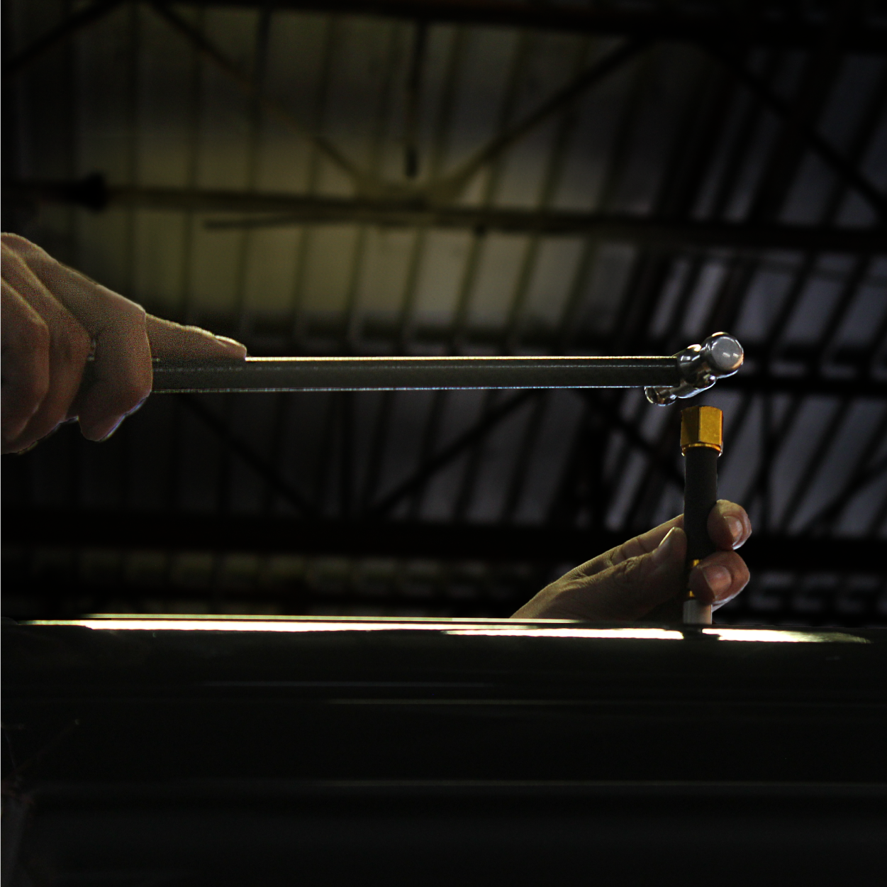 Hands using a wrench to tighten a bolt on a dark metal surface in a workshop