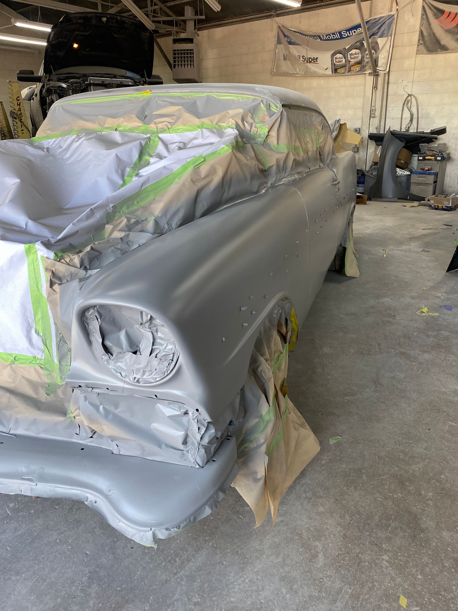 Classic car in a workshop, primed and masked for painting. Grey car body with green tape.