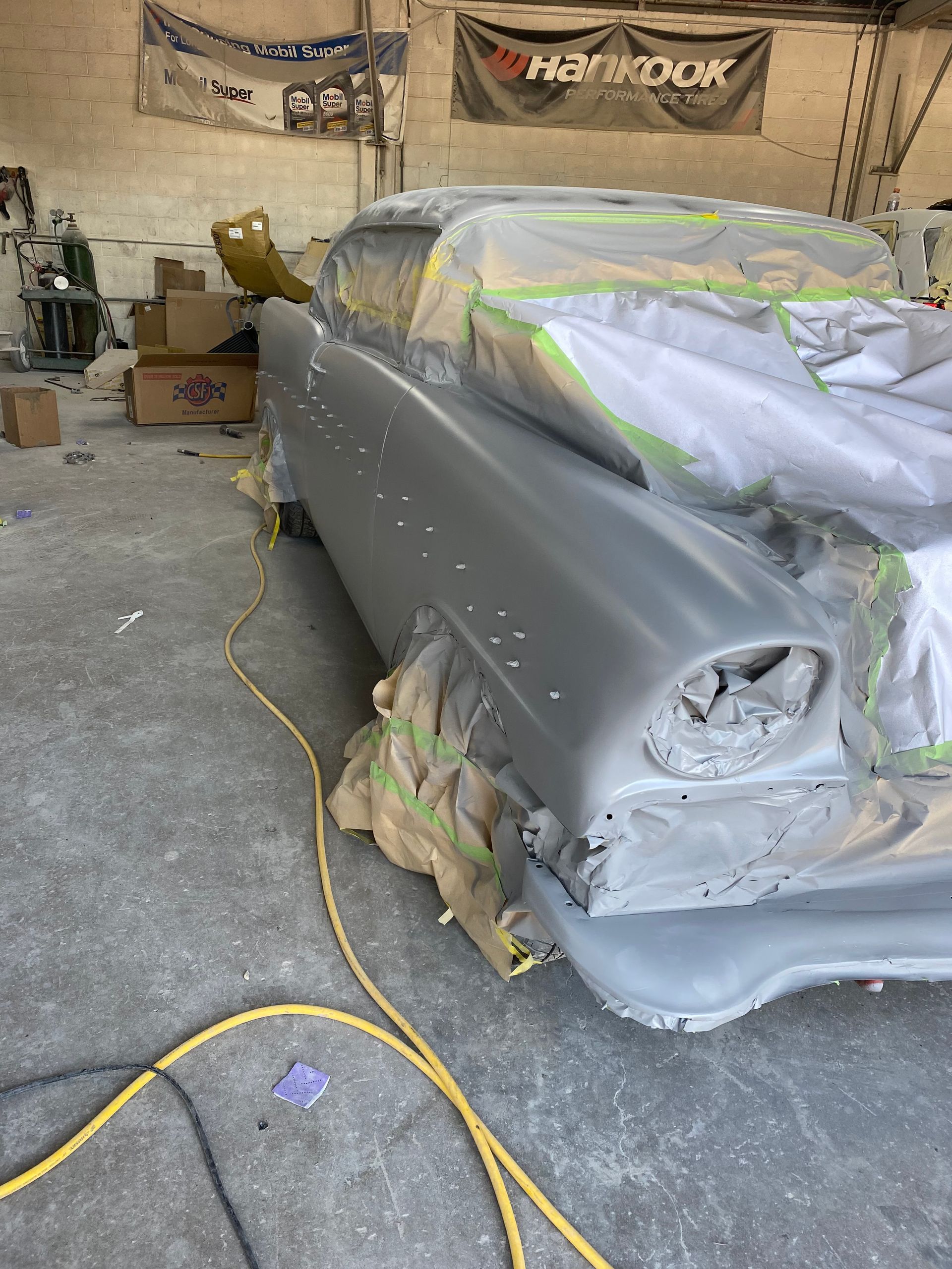 Classic car in a body shop, partially masked for painting.