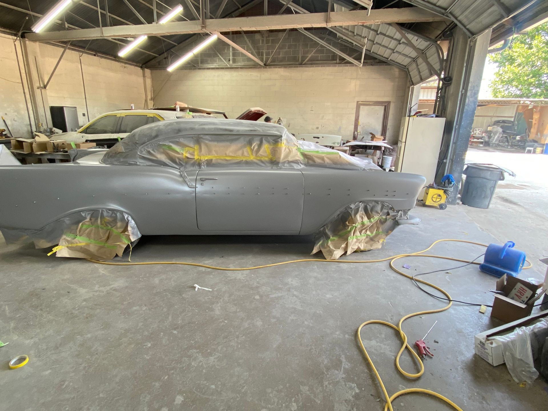 Classic car in primer, masked for painting, inside a garage.