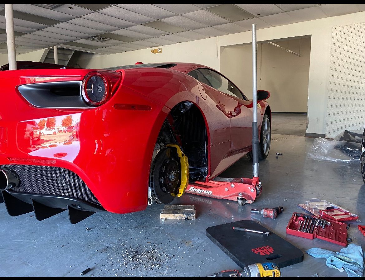 Red Ferrari sports car being worked on in a garage; rear wheel removed.