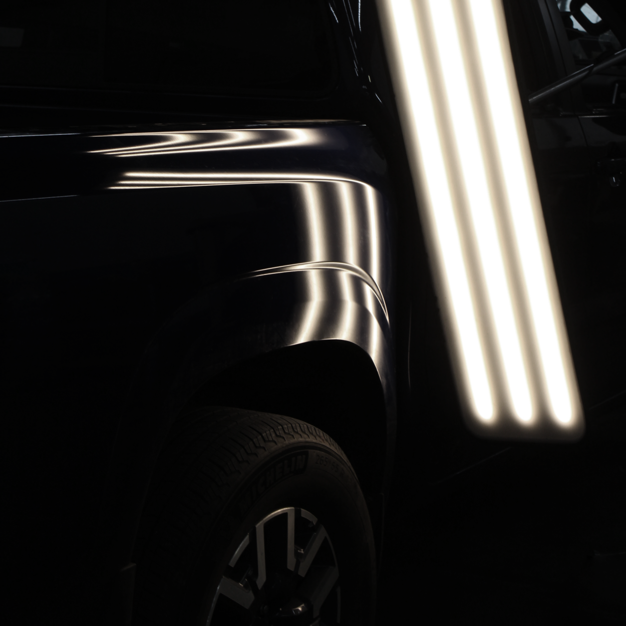 Close-up of a black car door reflecting bright vertical lights at night