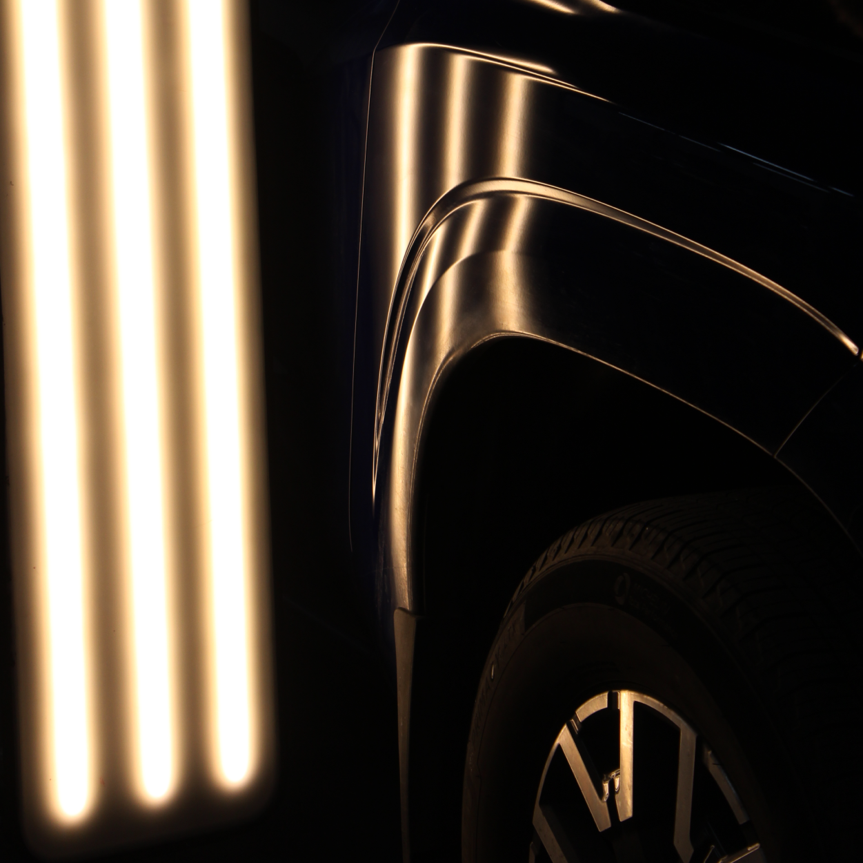 Close-up of a glossy black car with gold-lit vertical lights and a visible wheel rim