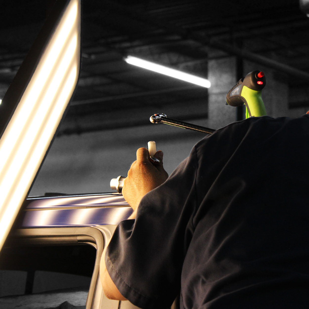 Person holding a device near a car roof under bright lights in a garage