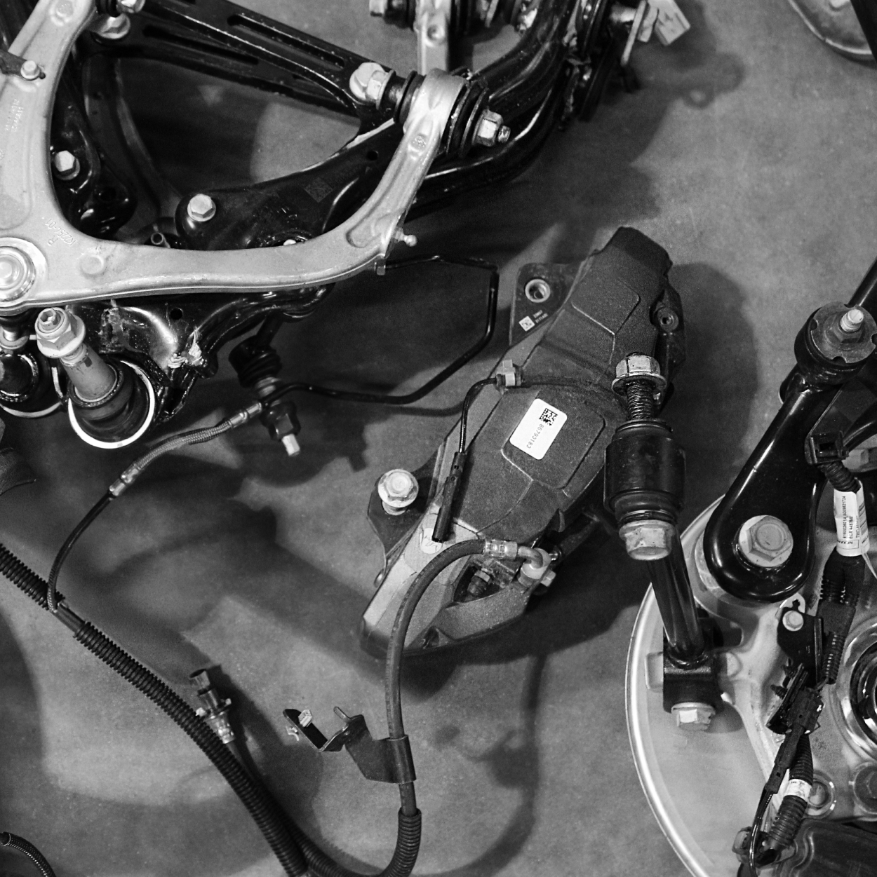 Black-and-white close-up of a mechanical assembly with wires, bolts, and connectors on a work surface
