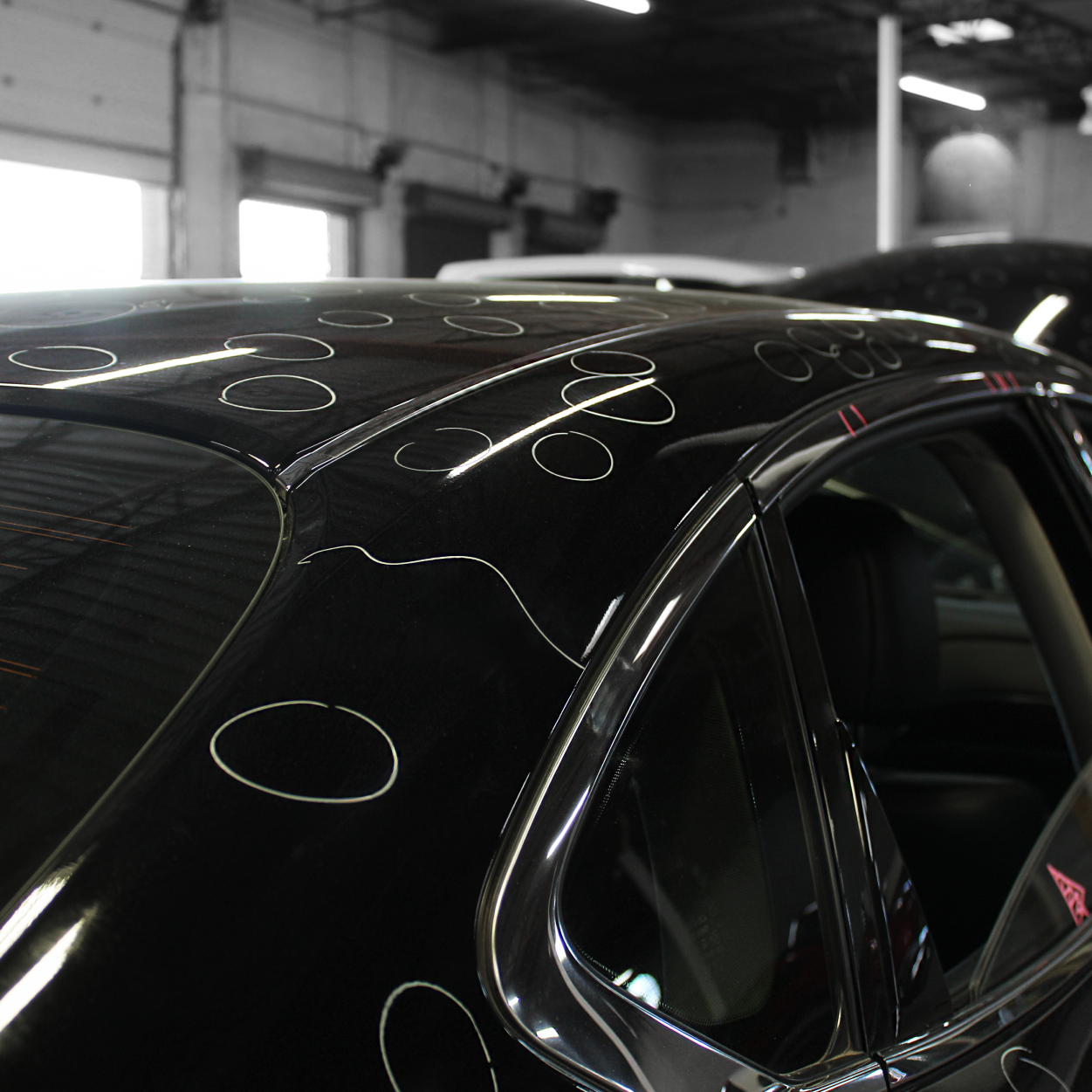 Black car roof with visible circular polish marks in a garage or workshop